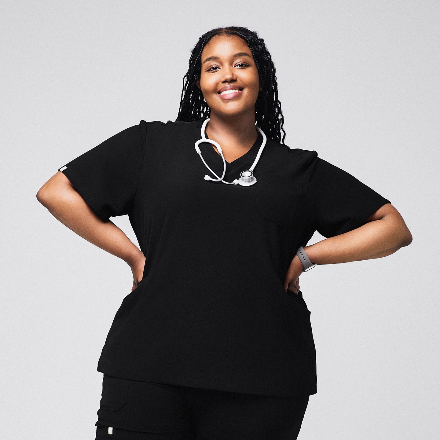 Female medical professional in a black scrub top with a stethoscope around her neck, standing with hands on her hips and smiling,Rich Black