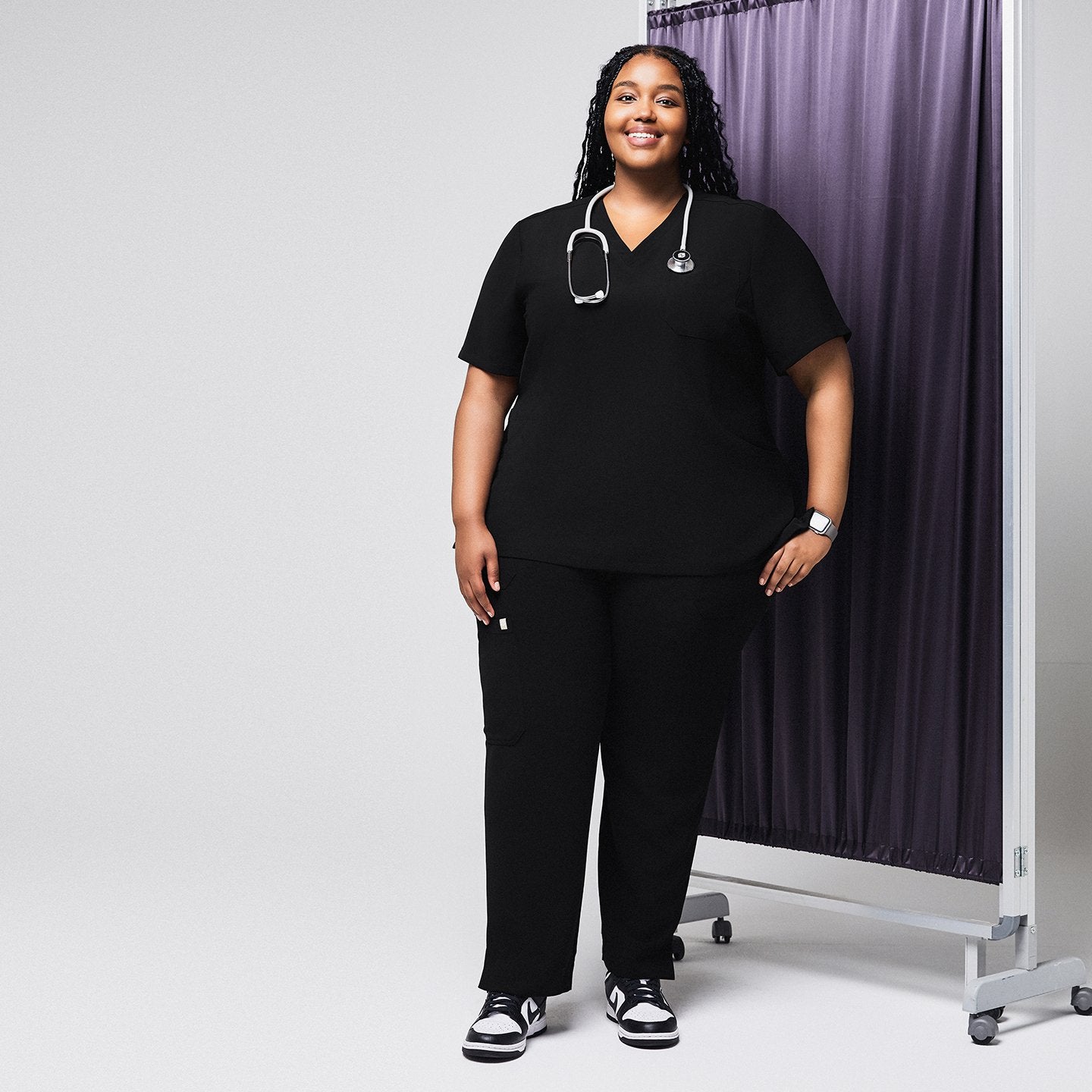 Model wearing the black scrub top and pants, with a stethoscope around her neck, standing in front of a purple privacy curtain,Rich Black