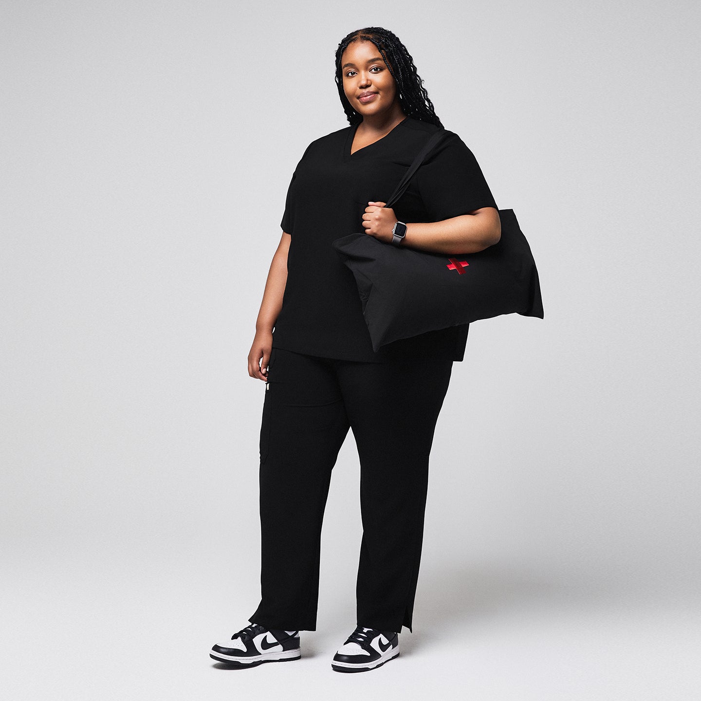 Woman wearing black scrubs with split hem pants, carrying a black bag with a red cross, paired with black and white sneakers,Rich-Black