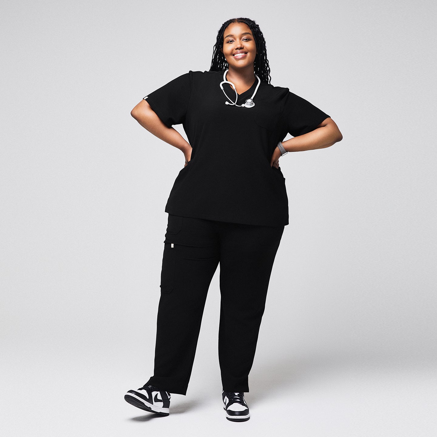 Smiling woman wearing black scrubs with split hem pants and a stethoscope around her neck, paired with black and white sneakers,Rich-Black