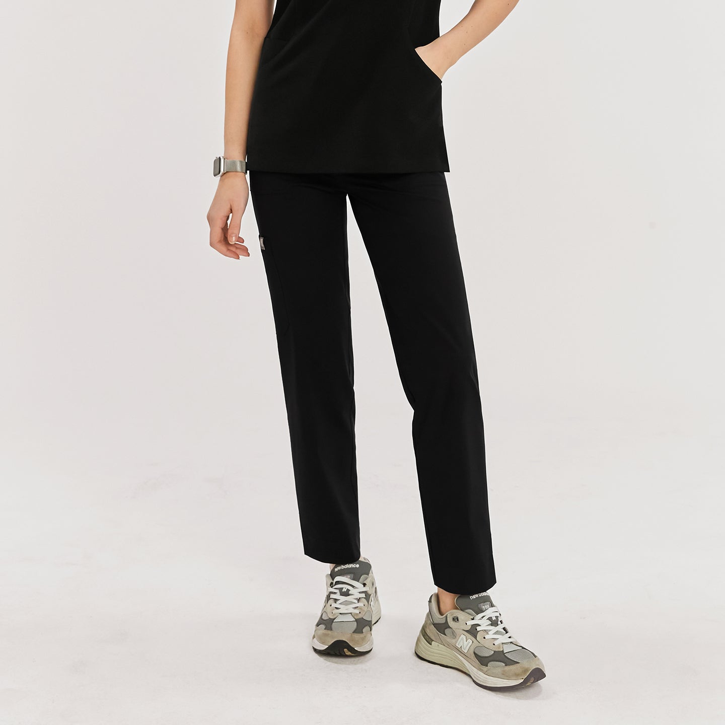 Woman wearing black zipper slit scrub pants with side pockets, paired with gray New Balance sneakers, in a front view,Rich Black