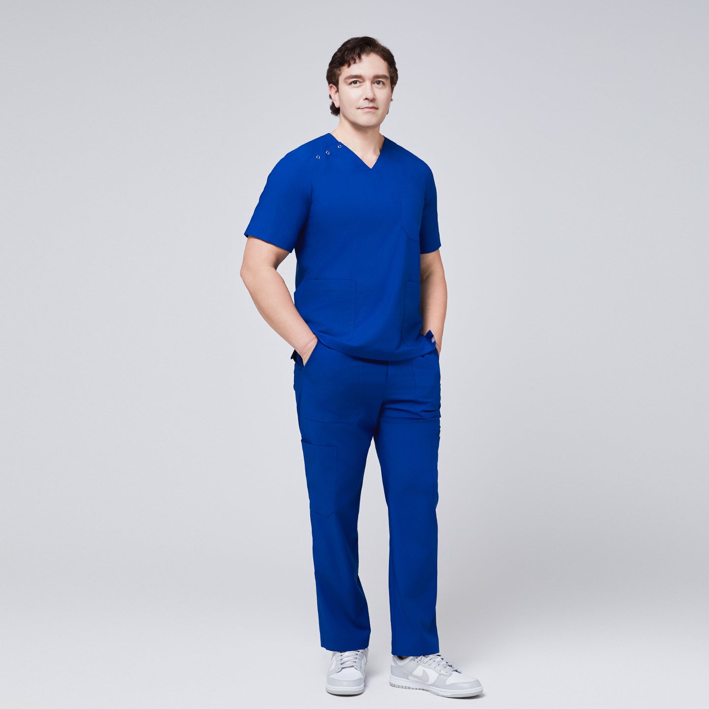 Man wearing Zenir royal blue 3-button scrub set with hands in pockets, paired with white sneakers,Royal Blue