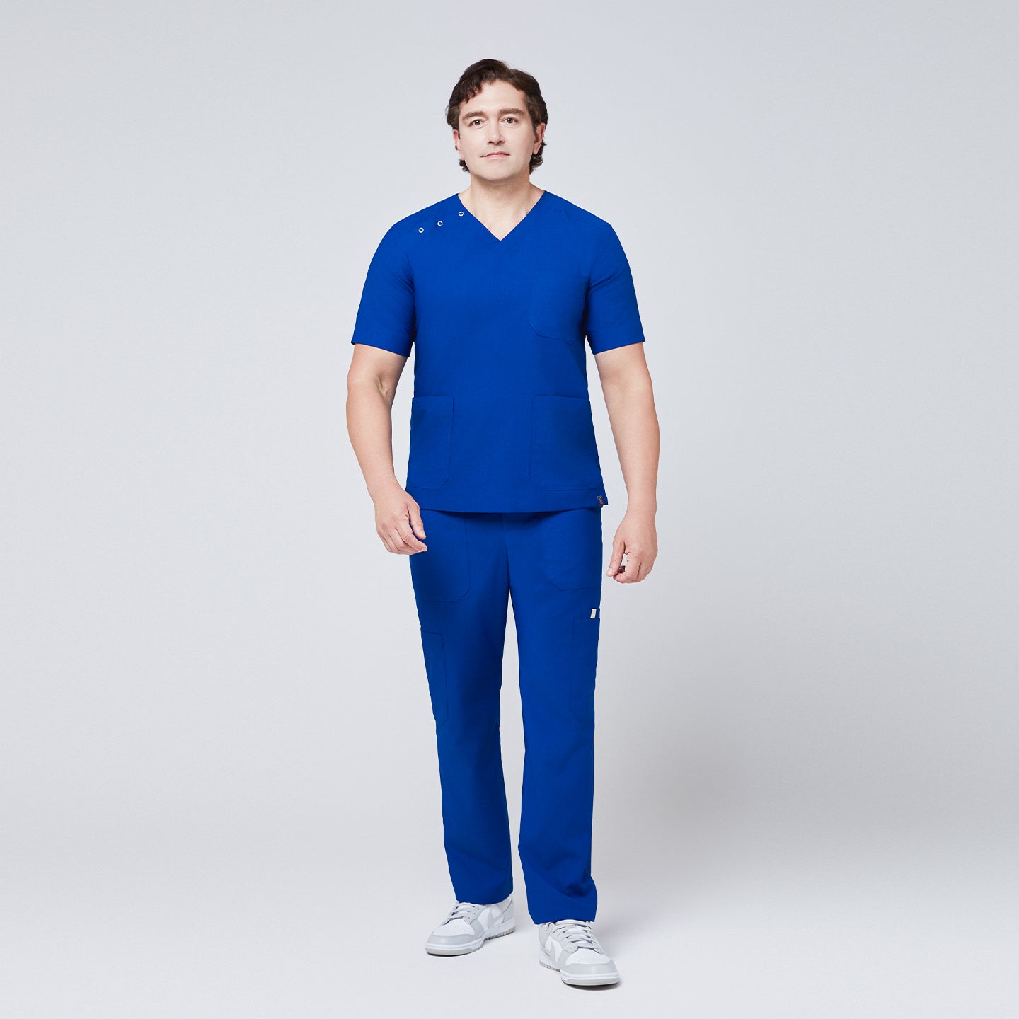 Man wearing Zenir royal blue 3-button scrub set with chest and lower pockets, paired with white sneakers,Royal Blue