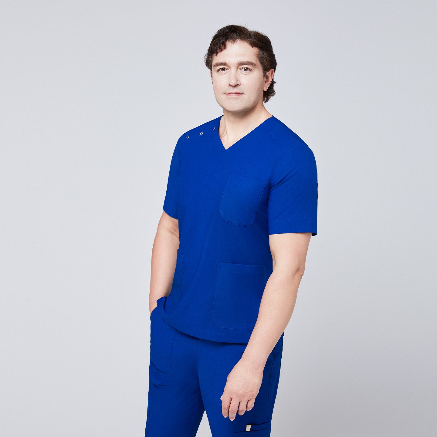 Man wearing Zenir royal blue 3-button scrub top with hands in pockets, featuring chest and lower pockets,Royal Blue