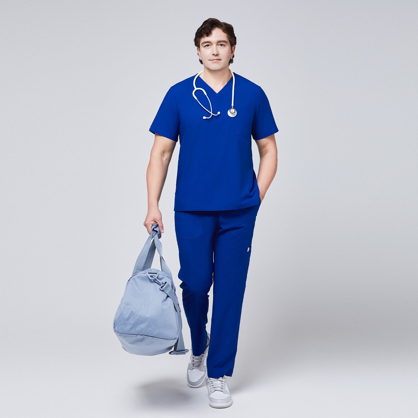 Man wearing a royal blue V-neck scrub top with matching pants, carrying a light blue duffel bag and wearing a stethoscope around his neck,Royal Blue