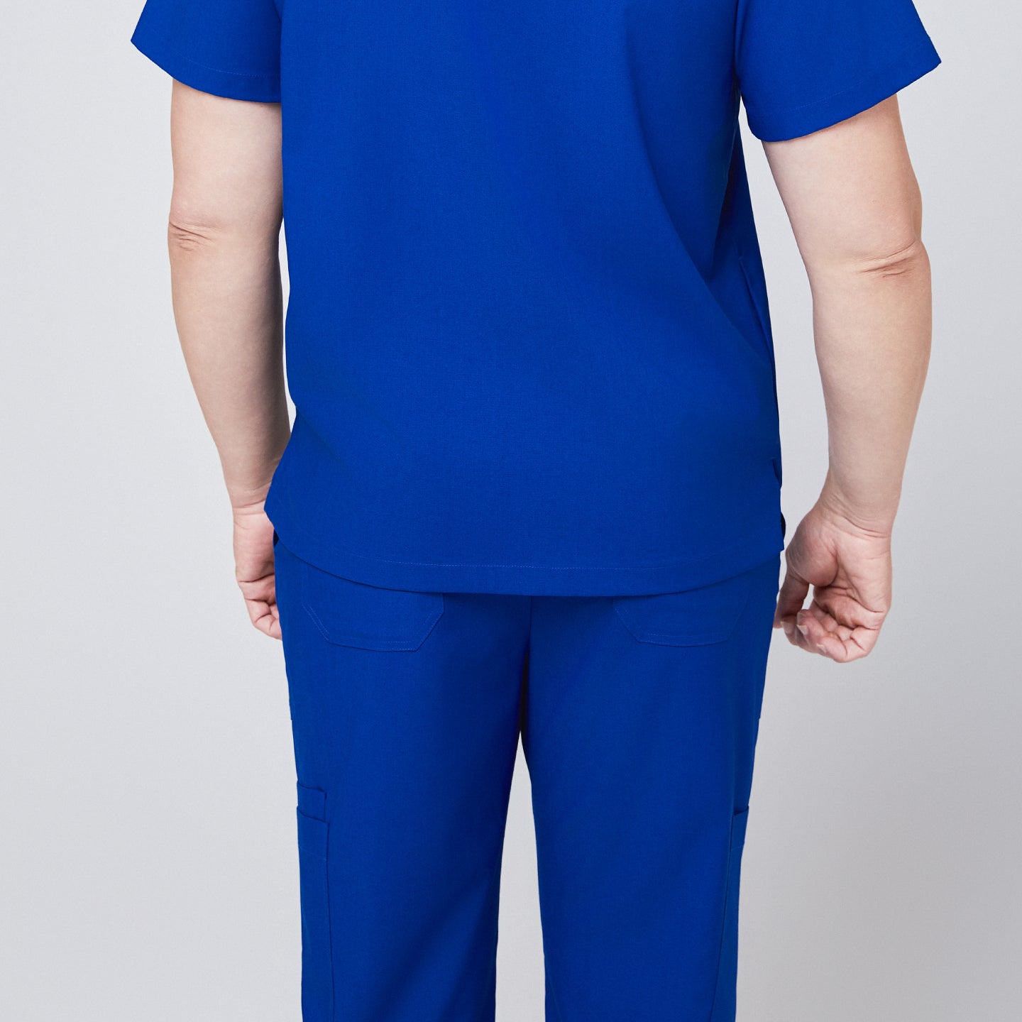 Back view of a person wearing royal blue scrub top and pants, showcasing the rear design of the uniform with pocket details,Royal Blue