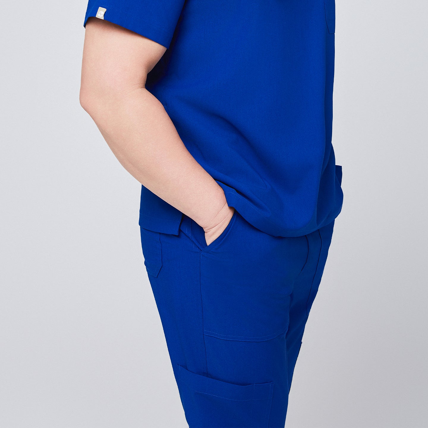 Side view of royal blue scrub pants with functional pockets, paired with a matching scrub top and hand in pocket,Royal Blue