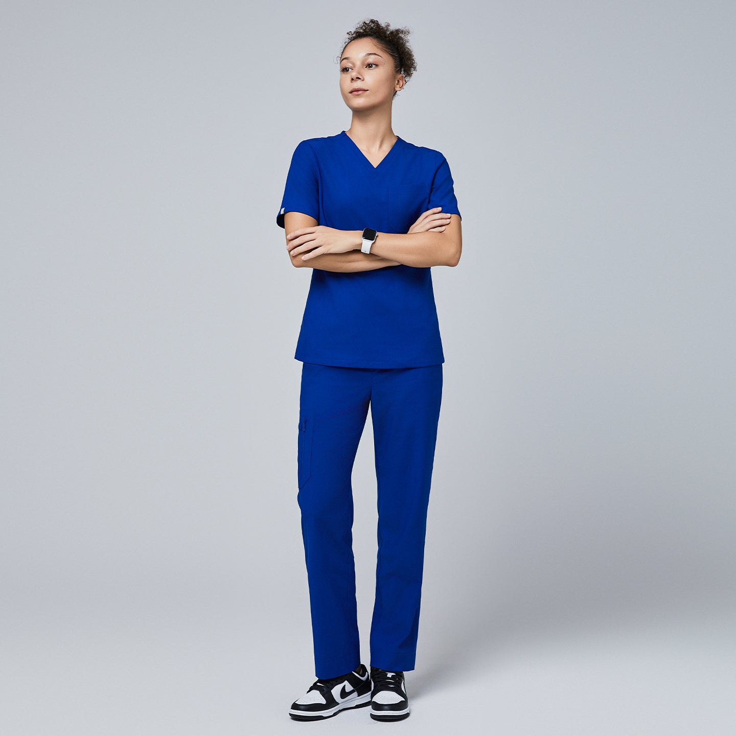 Model wearing a royal blue V-neck scrub set featuring a short-sleeve top and split-hem pants with zipper pockets, paired with black sneakers for a sleek and professional look,Royal Blue