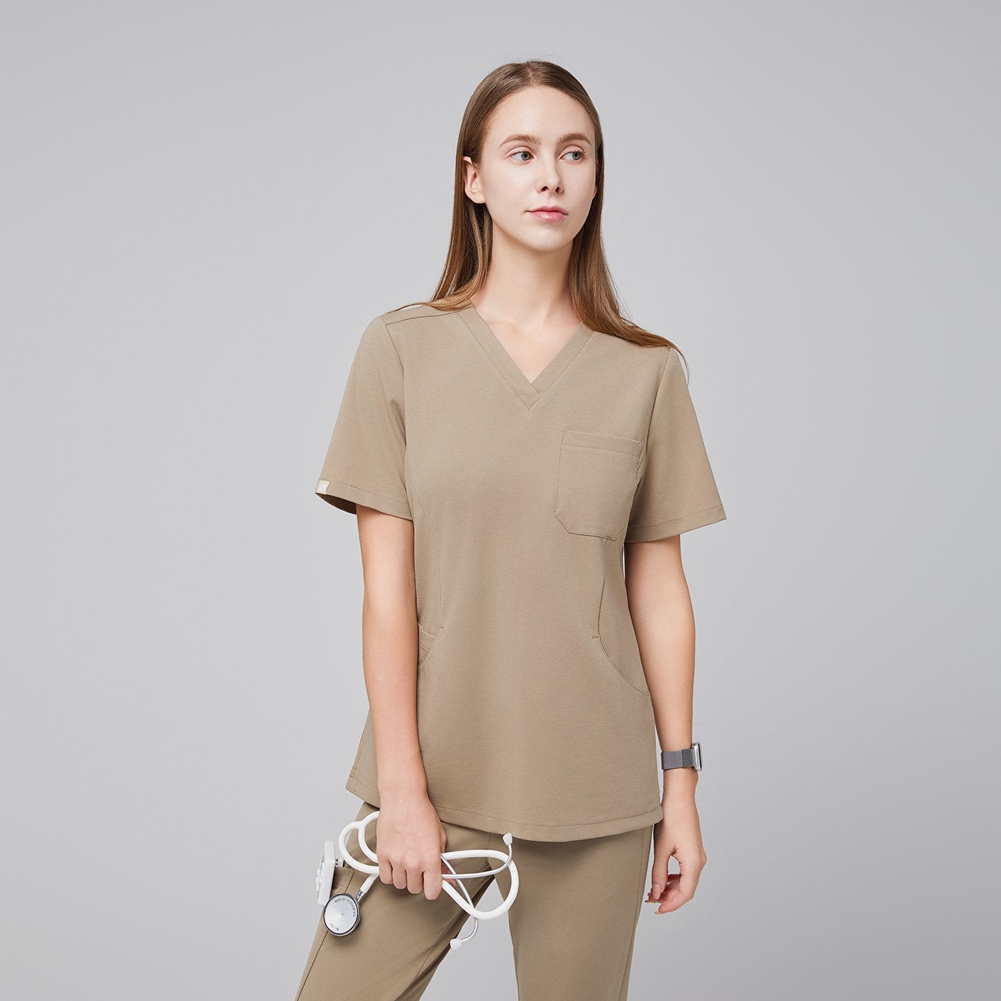 Female model wearing the Sand Beige Soft Stretch Scrub Top and scrub bottom, holding a stethoscope against a neutral gray background,Sand beige