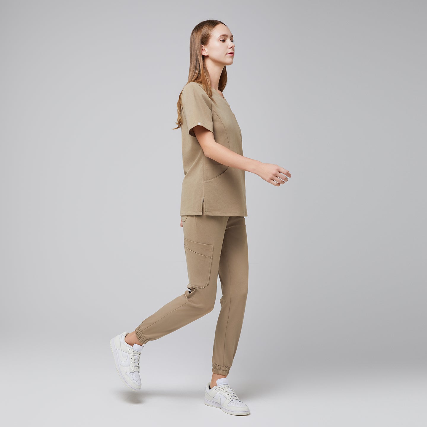 Scrub set featuring a V-neck top with side slits and jogger-style pants with cargo pockets, captured in a walking pose,Sand Beige