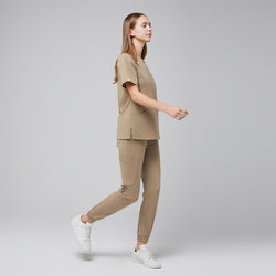 Image of Scrub set featuring a V-neck top with side slits and jogger-style pants with cargo pockets, captured in a walking pose,Sand Beige