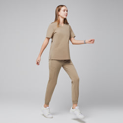 Image of Female wearing sand beige jogger scrub pants and top, walking in a side view, paired with white sneakers,Sand Beige