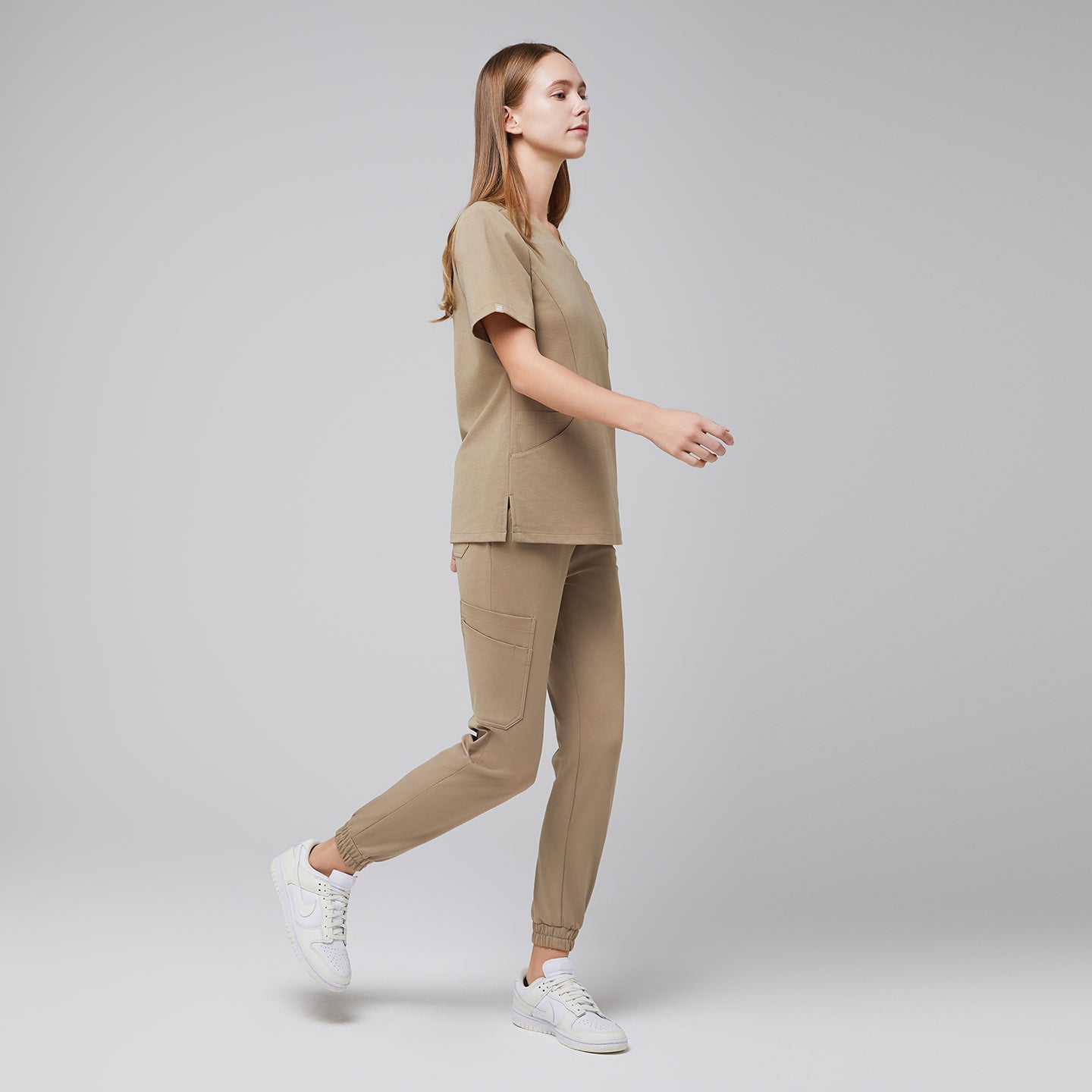 Side view of a woman wearing sand beige jogger scrubs with side pockets, paired with white sneakers,Sand Beige