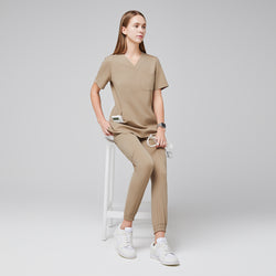 Image of Female wearing sand beige scrub top and jogger pants, sitting on a white stool, holding a stethoscope, paired with white sneakers,Sand Beige