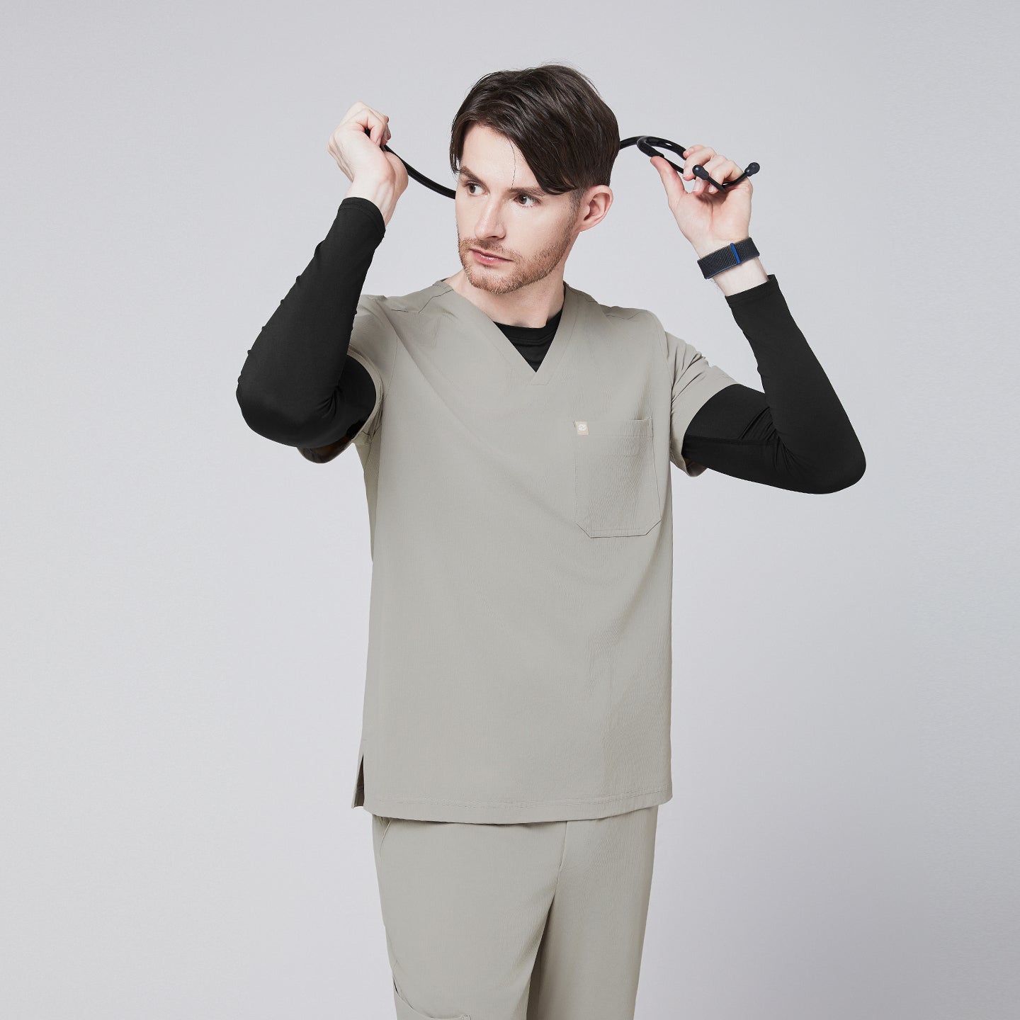 Male model wearing a sand khaki V-neck single-pocket scrub top, adjusting a stethoscope,Sand Khaki