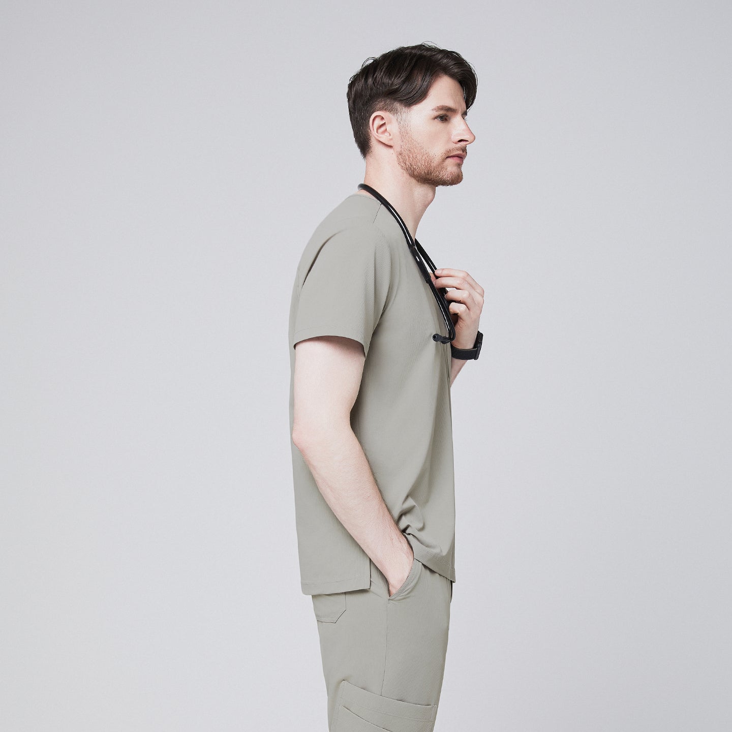 Male model in a sand khaki V-neck single-pocket scrub top, holding a stethoscope, side profile,Sand Khaki