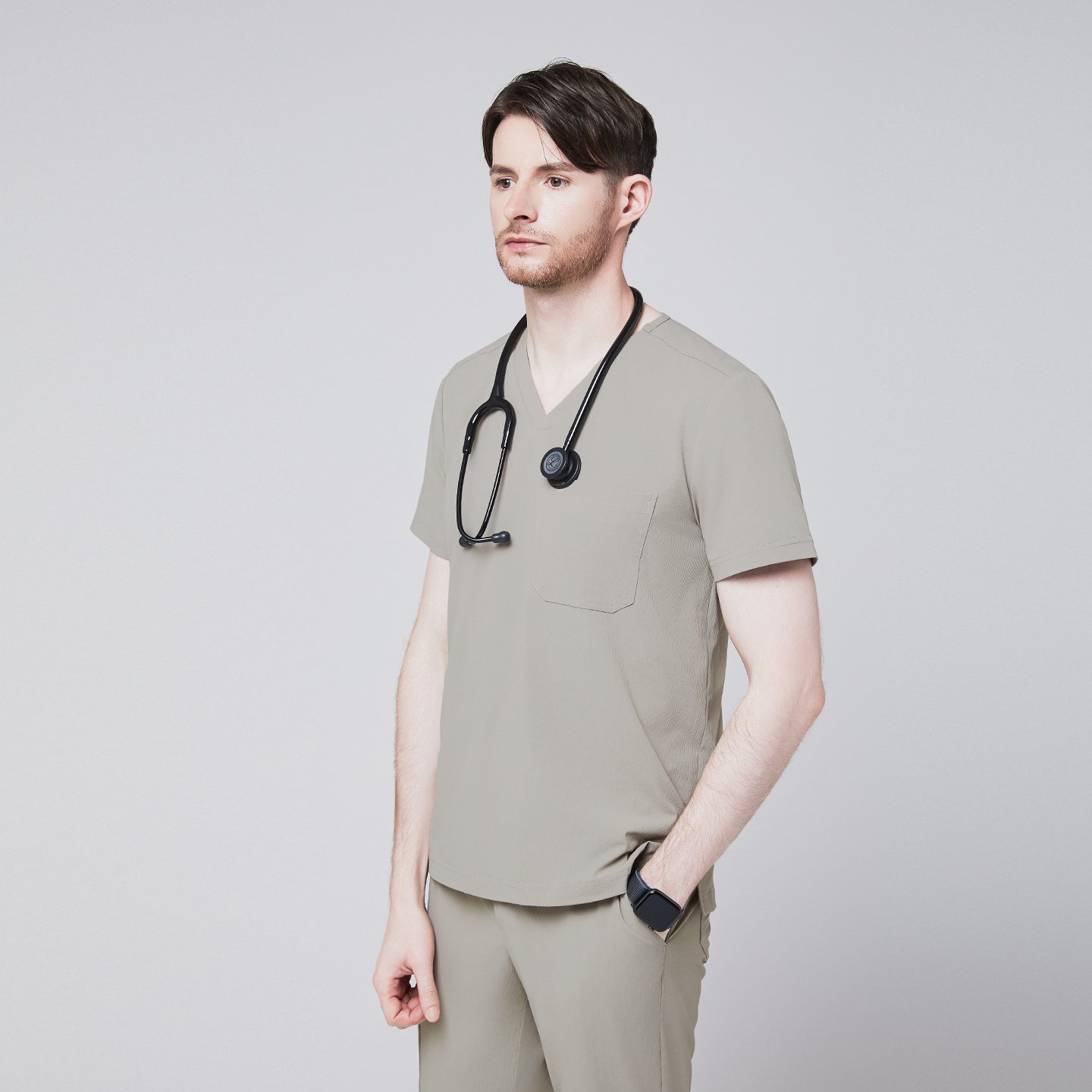 A man wearing a Sand Khaki Single Pocket Scrub Top and matching StretchFit Jogger Scrub Pants, holding a stethoscope at his chest,Sand Khaki