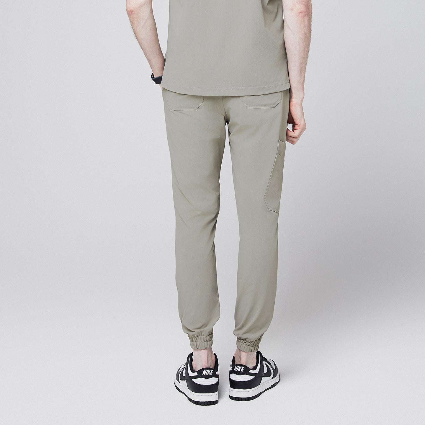 Back view of sand khaki jogger scrub pants with elastic cuffs and back pockets, paired with black and white sneakers,Sand Khaki