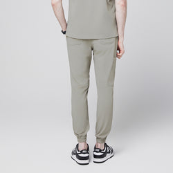 Image of Back view of sand khaki jogger scrub pants with elastic cuffs and back pockets, paired with black and white sneakers,Sand Khaki