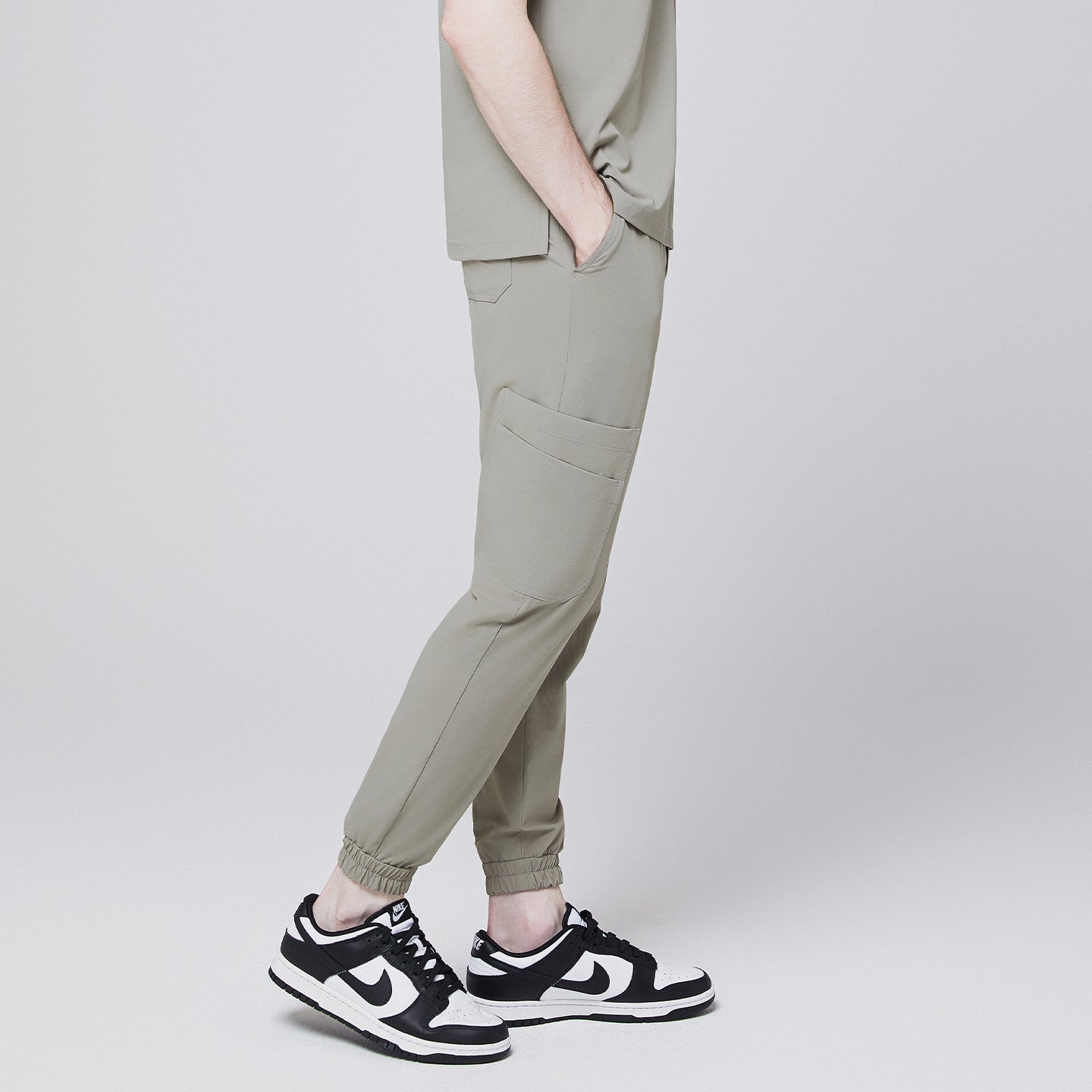 Side view of sand khaki jogger scrub pants with elastic cuffs and side pocket, styled with black and white sneakers,Sand Khaki