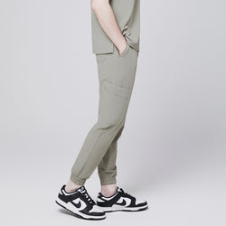 Image of Side view of sand khaki jogger scrub pants with elastic cuffs and side pocket, styled with black and white sneakers,Sand Khaki