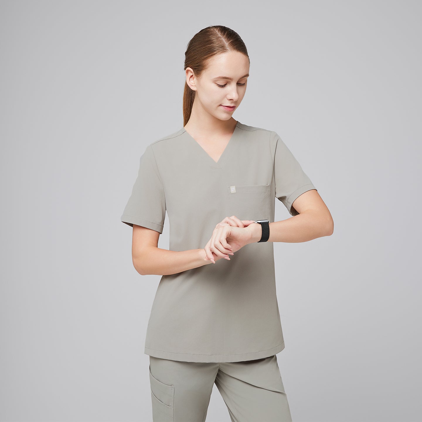 Female healthcare professional in a sand khaki scrub top and pants, checking the time on a smartwatch,Sand Khaki