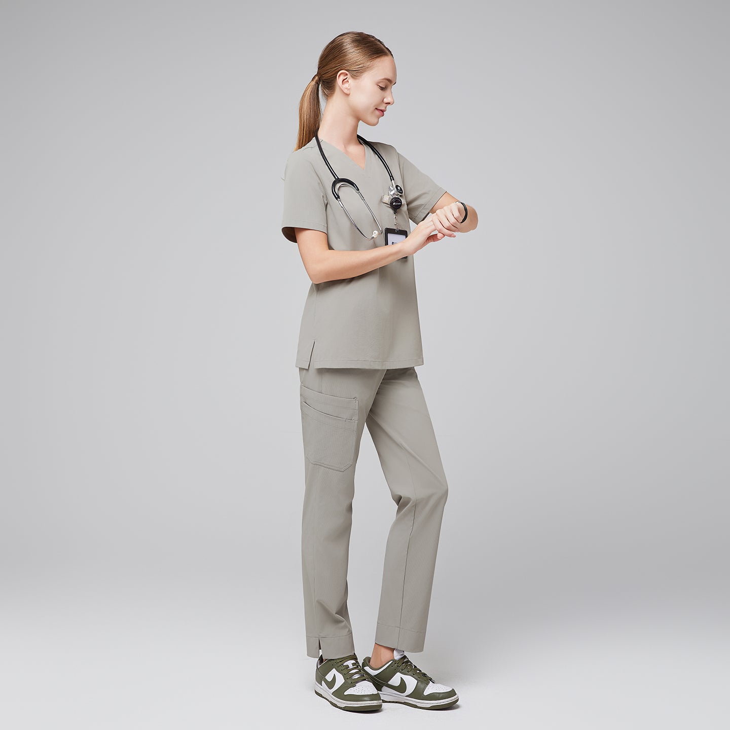 Female healthcare professional in a sand khaki scrub set, wearing a stethoscope and checking the time on a smartwatch, full-body side view,Sand Khaki