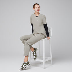 Image of Female healthcare professional sitting on a white chair, wearing a sand khaki scrub set with a black undershirt and green sneakers,Sand Khaki