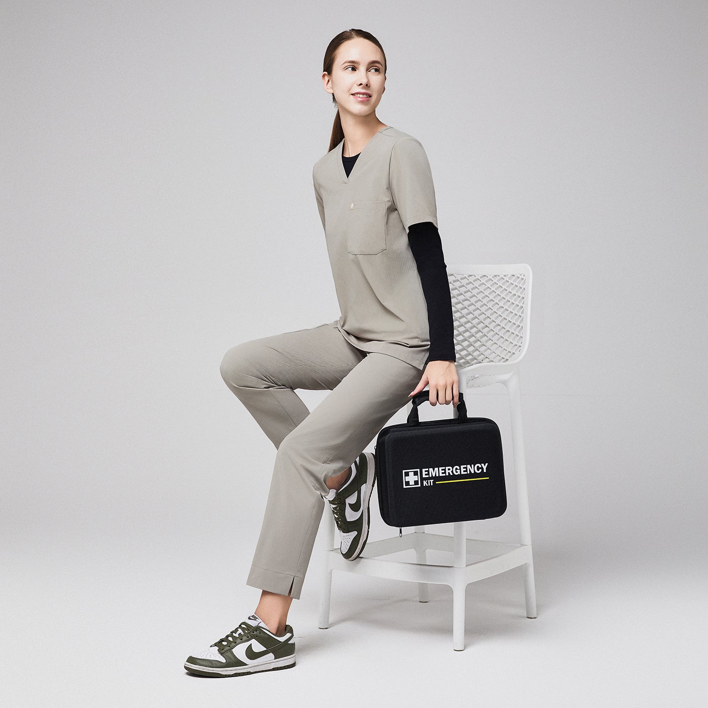 Female healthcare professional in khaki scrubs sitting on a chair, holding an emergency kit,Sand Khaki