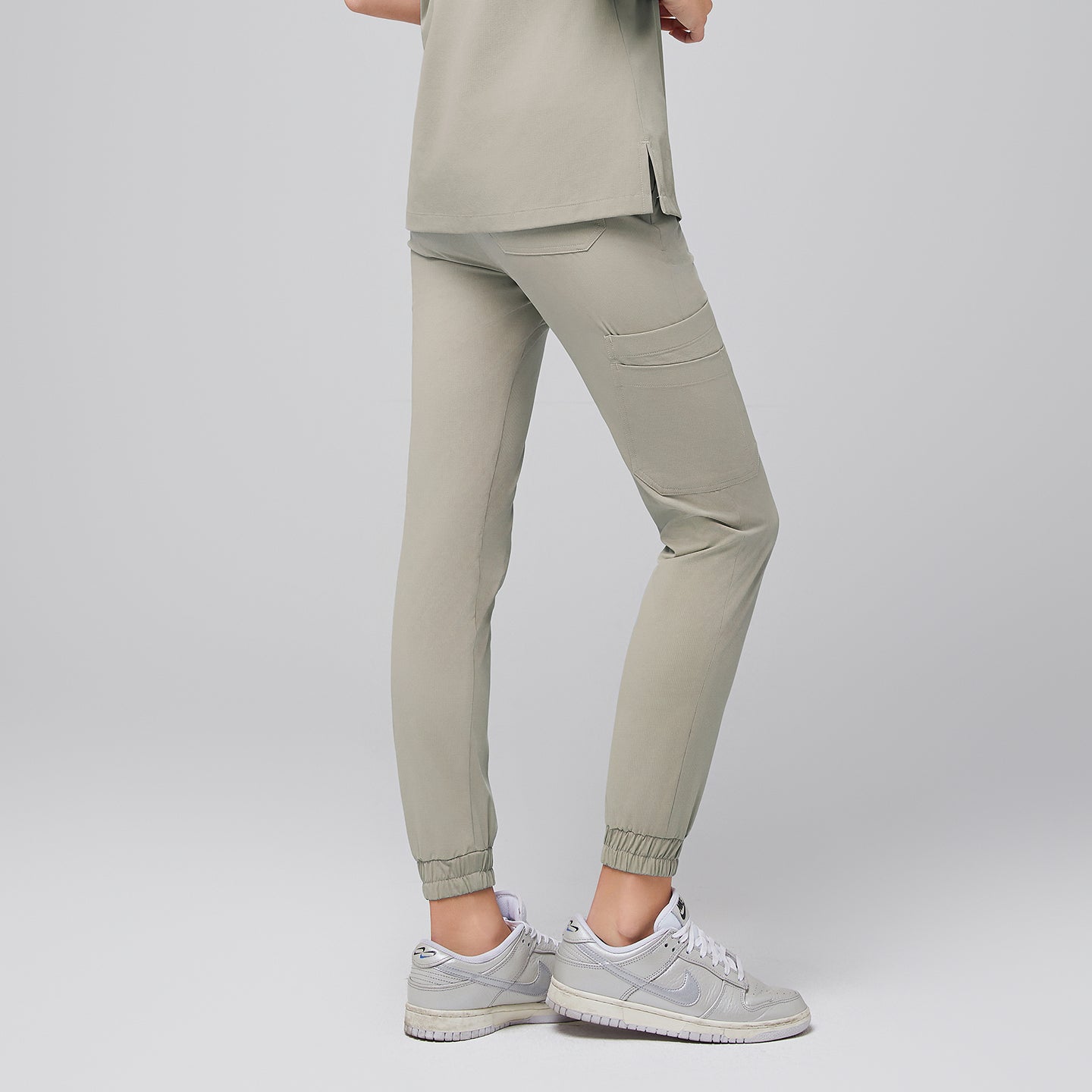 Back view of sand khaki jogger scrub pants showcasing a tailored fit with back pockets and elasticized cuffs, paired with sleek silver sneakers for a modern and professional appearance, Sand Khaki