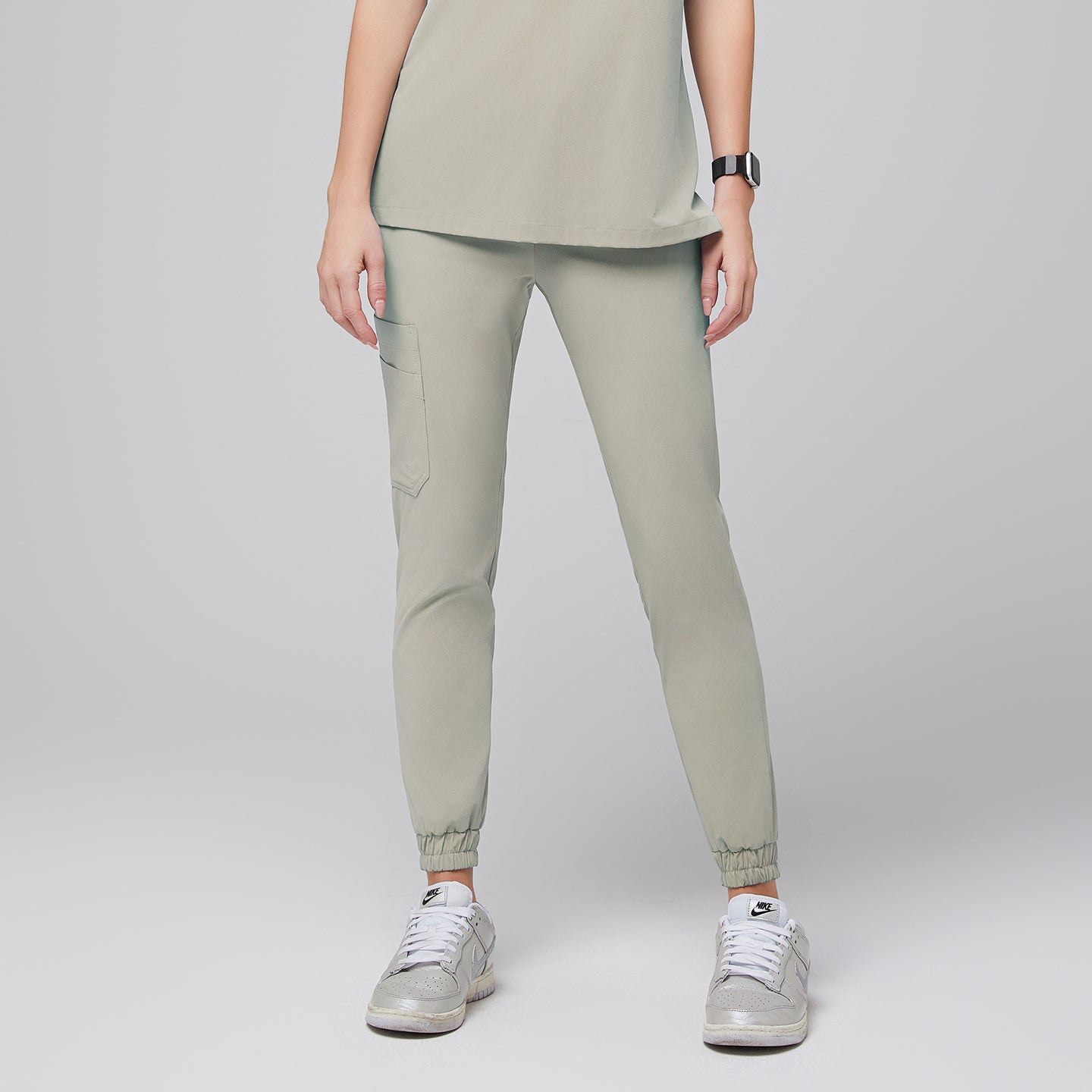 Front view of sand khaki jogger scrub pants featuring an elastic waistband, a side pocket, and cuffed hems, paired with silver sneakers for a stylish and functional look,Sand Khaki