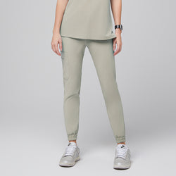 Image of Front view of sand khaki jogger scrub pants featuring an elastic waistband, a side pocket, and cuffed hems, paired with silver sneakers for a stylish and functional look,Sand Khaki