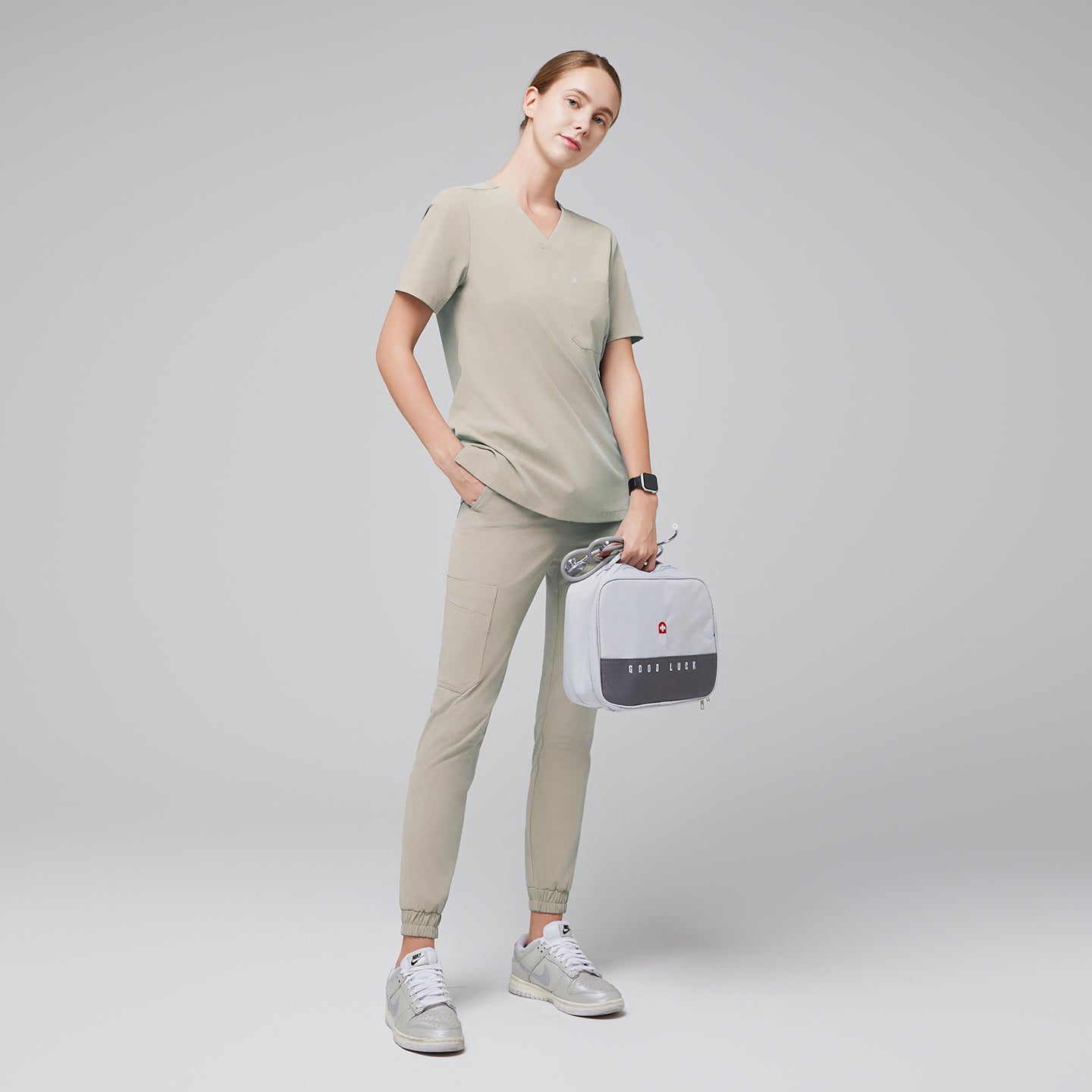 Full-body view of a model wearing sand khaki jogger scrub pants and a matching scrub top, accessorized with a gray medical bag and silver sneakers, presenting a professional and comfortable outfit, Samd Khaki