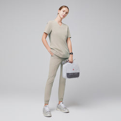 Image of Full-body view of a model wearing sand khaki jogger scrub pants and a matching scrub top, accessorized with a gray medical bag and silver sneakers, presenting a professional and comfortable outfit, Samd Khaki