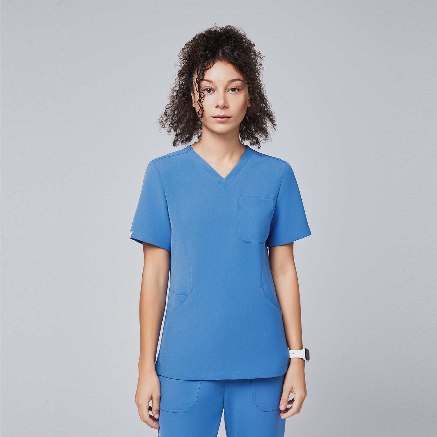 Front view of a woman wearing a sky-blue scrub top with a V-neck design and matching pants, presenting a comfortable and professional uniform style,Sky Blue