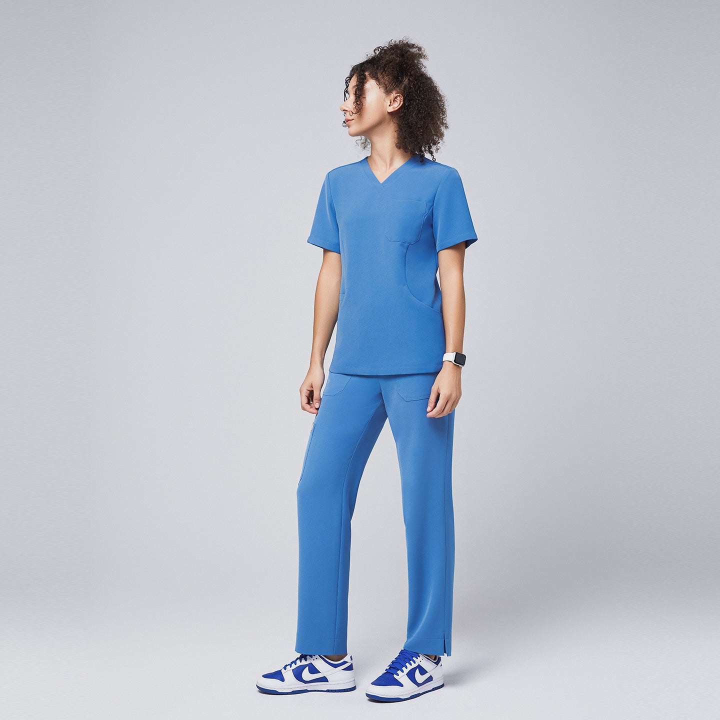 Side view of a woman wearing a sky-blue V-neck scrub top paired with matching straight-leg pants and blue sneakers, exuding a casual yet professional healthcare uniform style,Sky Blue