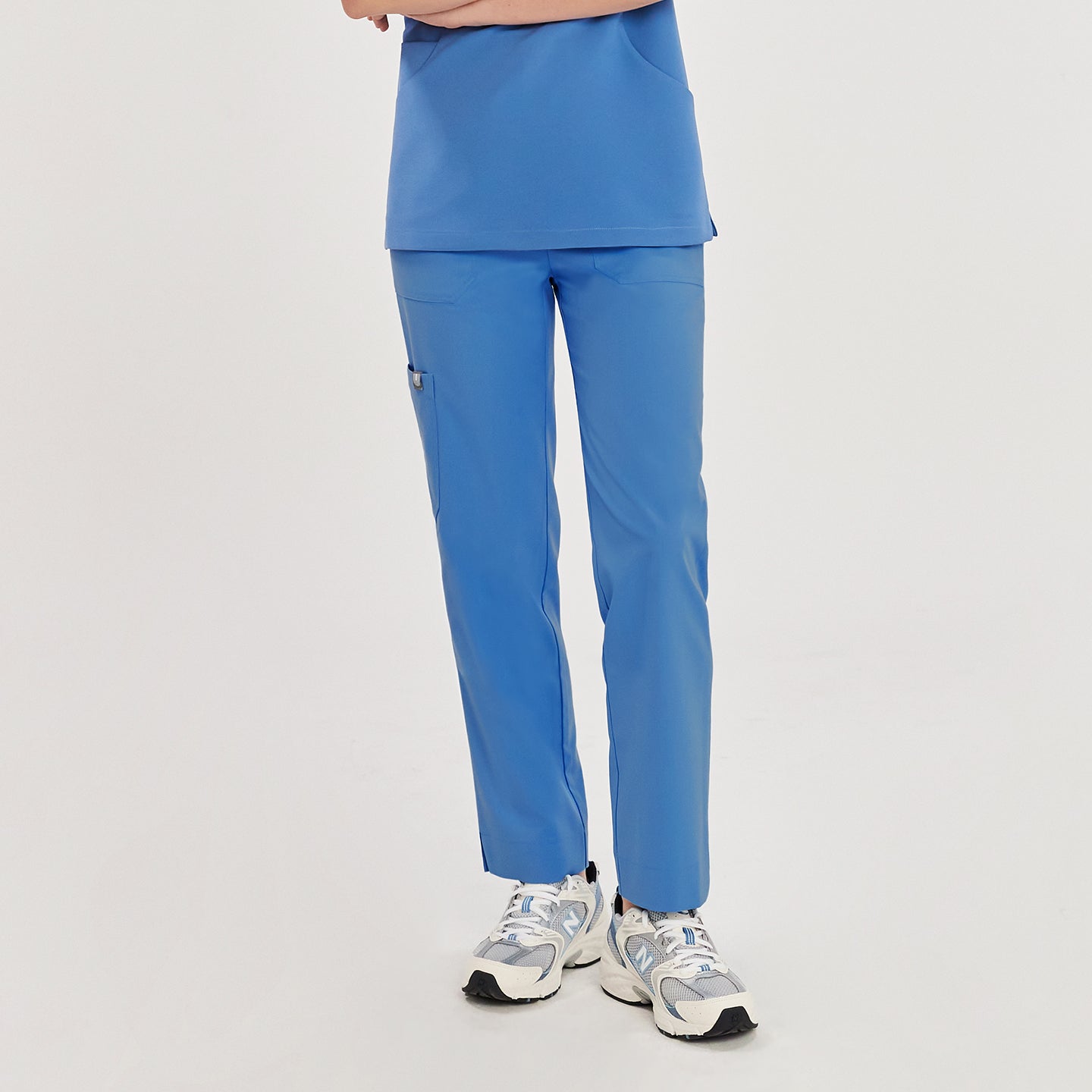Woman in sky blue zipper slit scrub pants with a side pocket and matching top, showing the pants from the front,Sky Blue