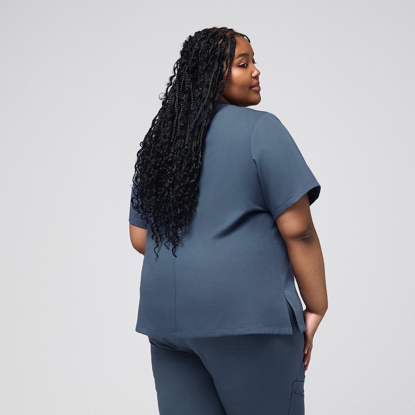 Plus-size healthcare professional in smoky blue scrub top, showing the back view with long curly hair cascading down,Smoky Blue