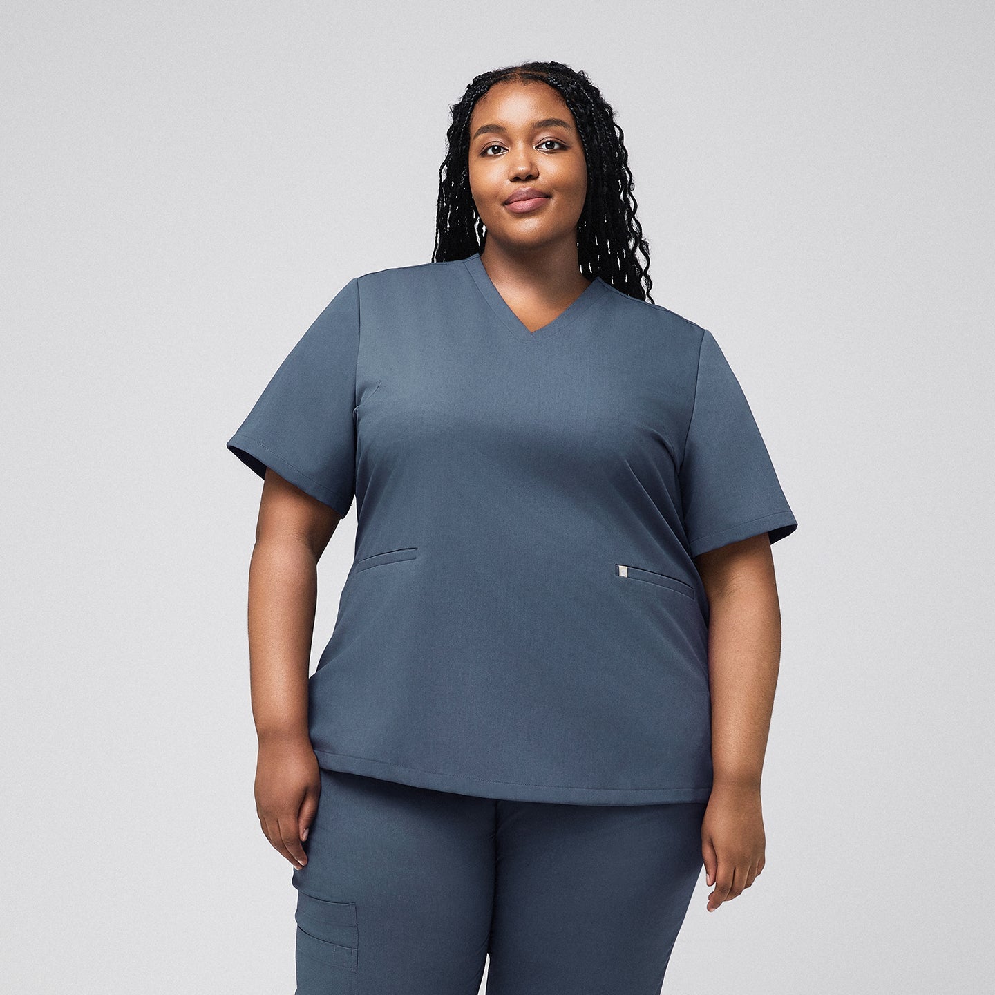 A woman wearing a Smoky Blue Double Pocket Scrub Top and matching scrub pants, standing in a relaxed pose,Smoky Blue