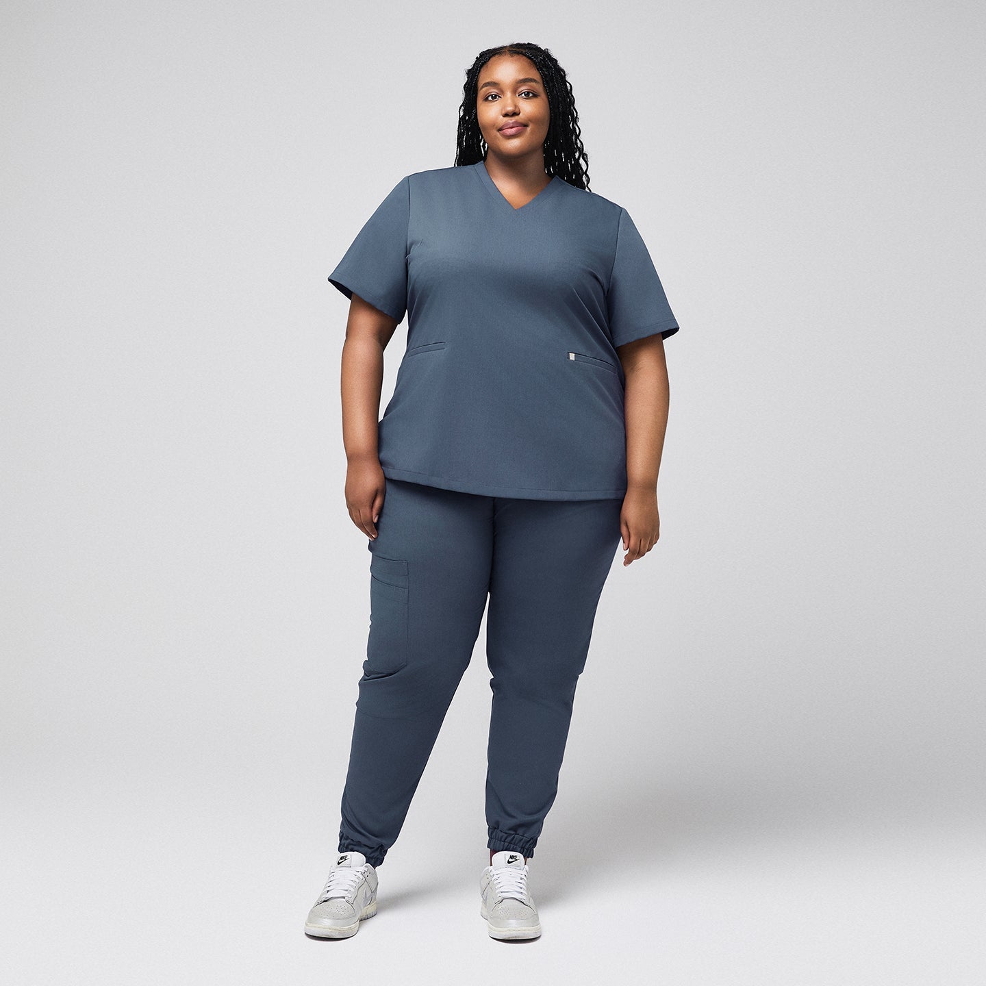 A woman wearing a Smoky Blue Double Pocket Scrub Top and matching scrub pants, shown in a full-body view,Smoky Blue