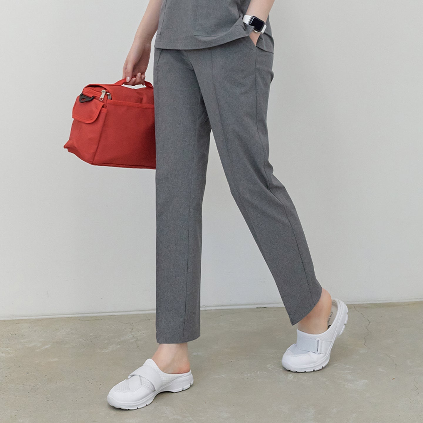 A woman wearing Soft Gray Line Banding Scrub Pants and a matching top, standing with a red bag, showcasing the full side view of the pants,Soft Gray