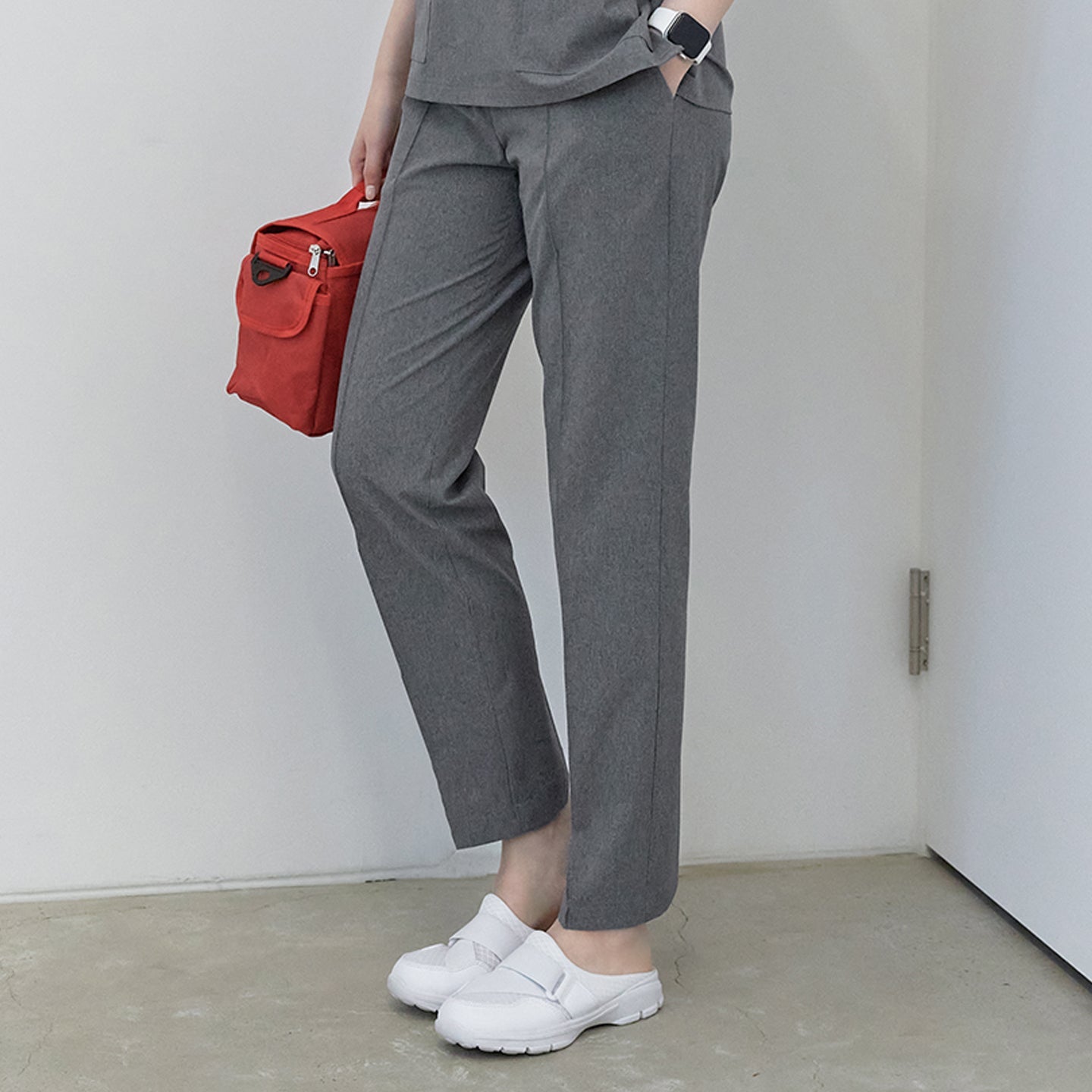 A woman holding a red bag, wearing Soft Gray Line Banding Scrub Pants and a matching top, showing the half side view of the pants,Soft Gray