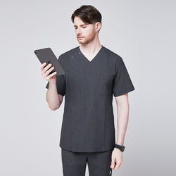 Image of Man wearing a soft gray scrub top with a V-neck and shoulder button detail, paired with matching pants, holding a tablet while glancing at it,Charcoal Gray