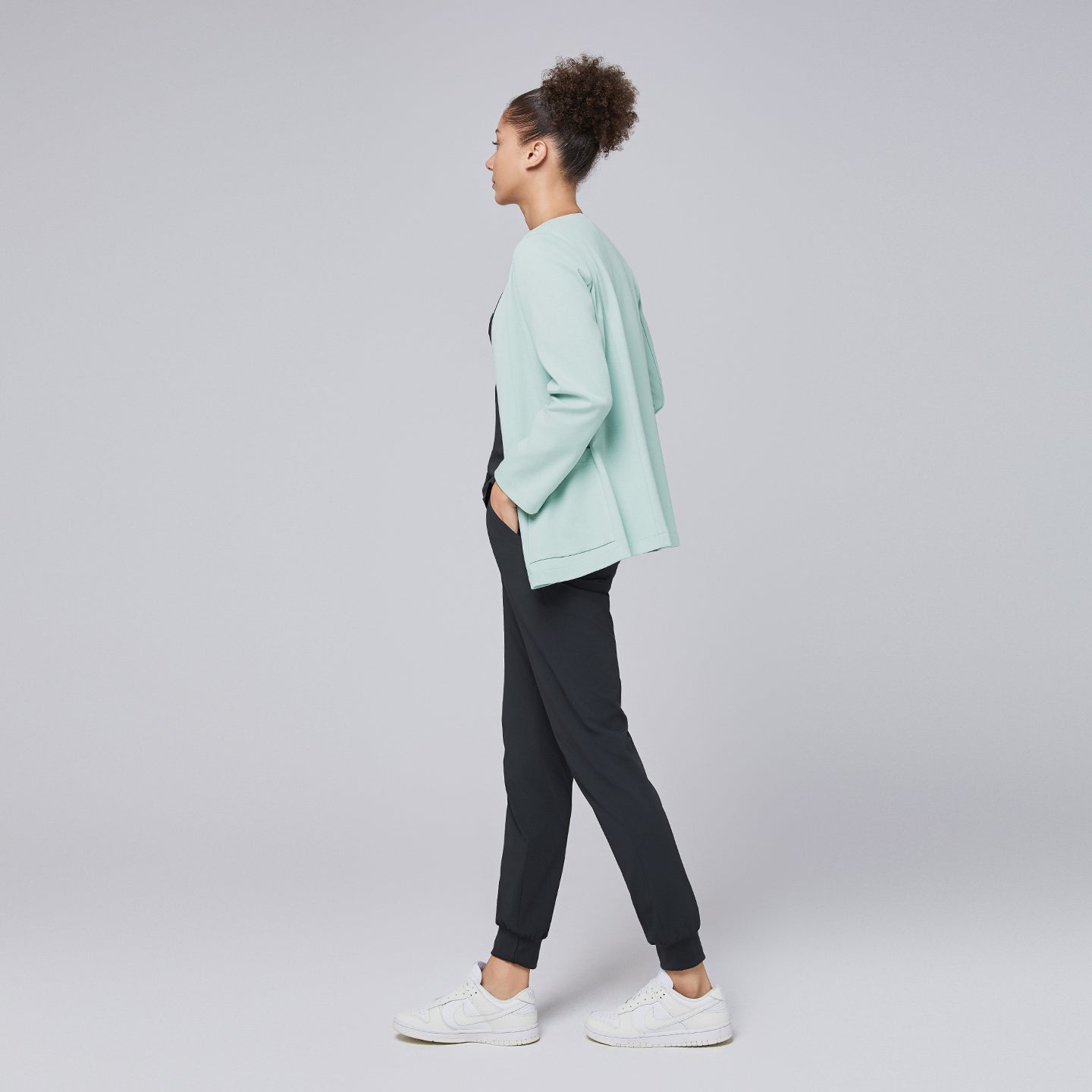 A side profile of a woman wearing a soft mint comfort cardigan paired with black jogger-style scrub pants and white sneakers, showcasing the cardigan's relaxed yet professional silhouette,Soft Mint