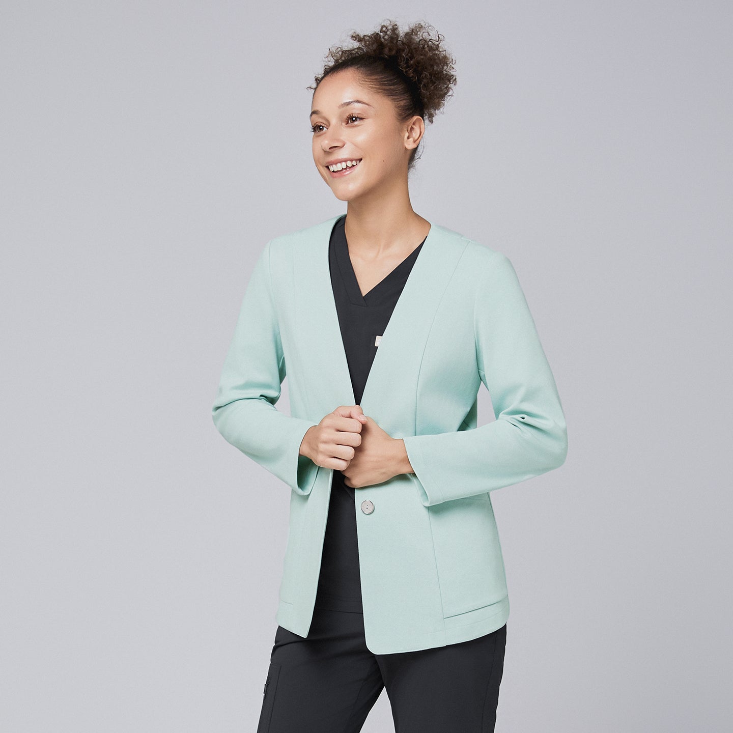 A smiling woman wearing a soft mint comfort cardigan over black scrubs, showcasing a polished and modern professional look,Soft Mint