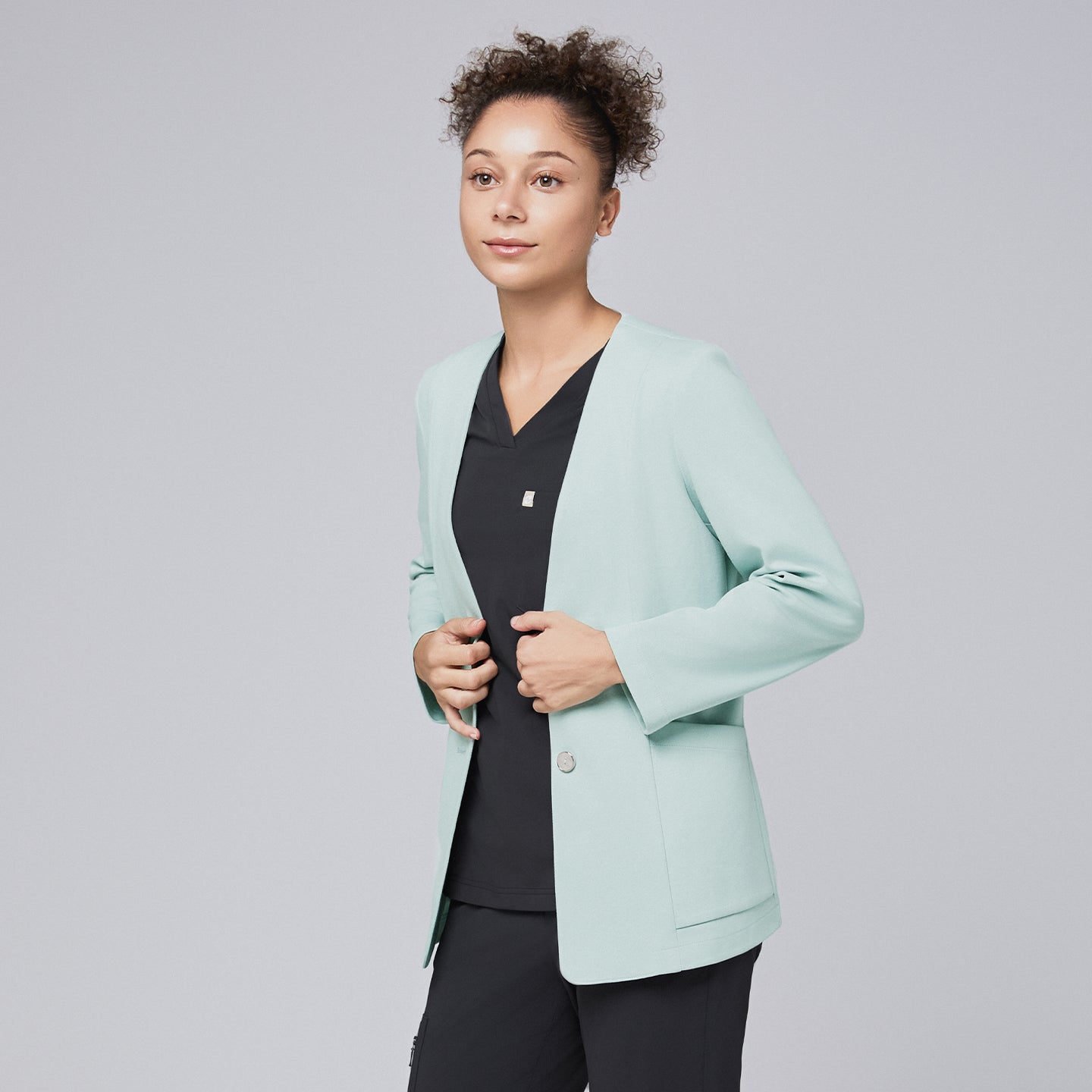 A professional woman wearing a soft mint comfort cardigan over a black scrub top, gently adjusting the cardigan's fit with a poised expression, highlighting its modern and polished design.Soft Mint