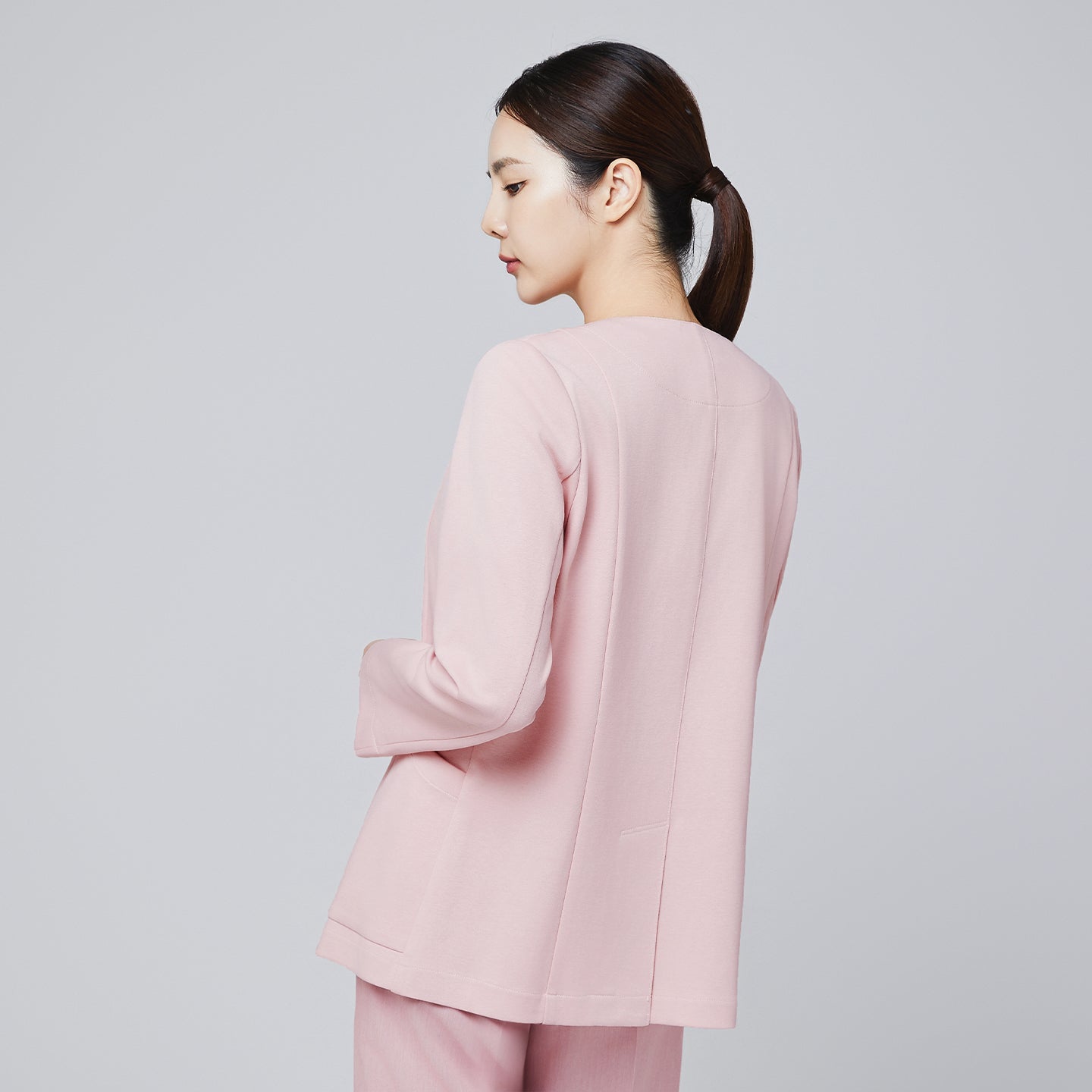 A woman seen from the back wearing a soft pink comfort cardigan, showcasing its clean back design and smooth fabric, paired with matching trousers,Soft Pink