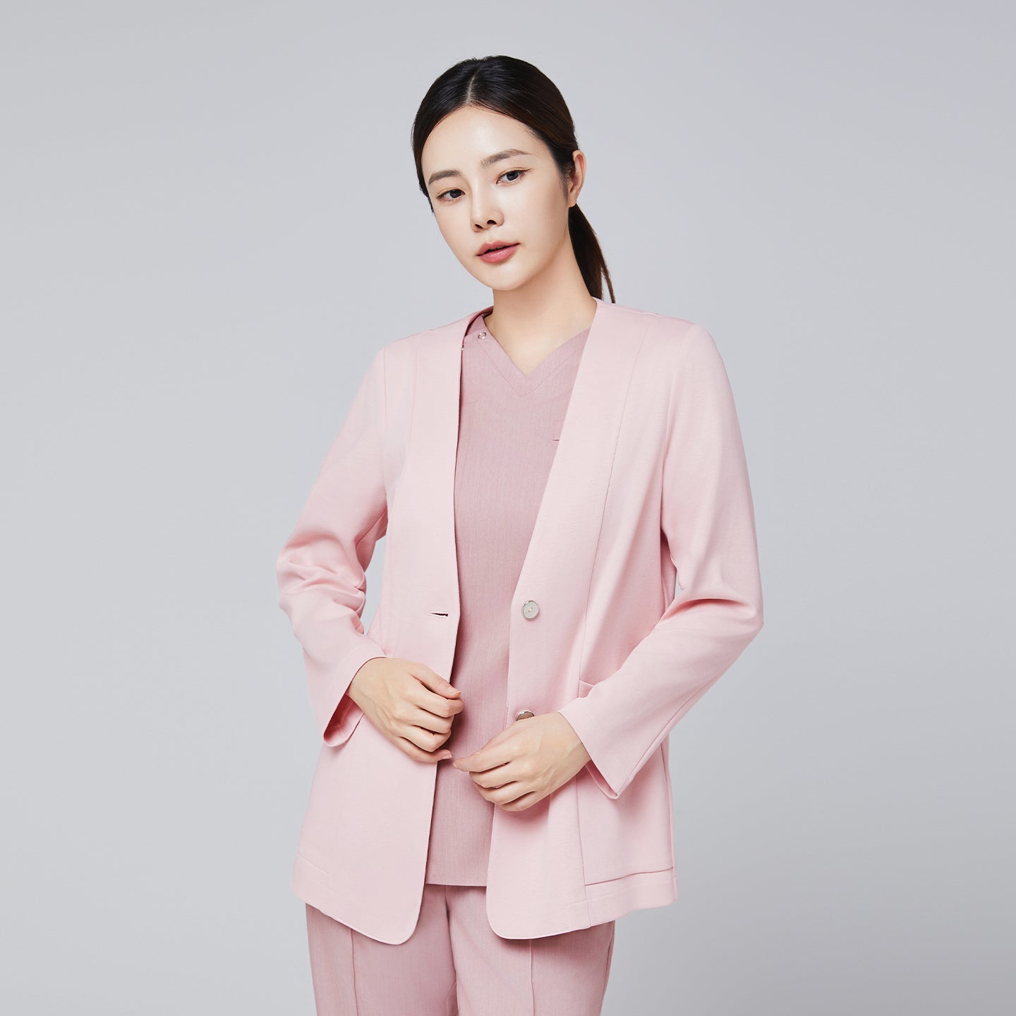 A woman dressed in a soft pink comfort cardigan featuring buttons, styled with a matching V-neck top and trousers, posing with her hands near the cardigan's hem against a plain background,Soft Pink