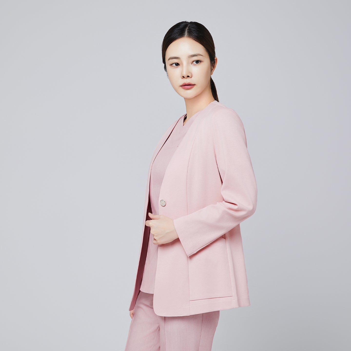 A woman wearing a soft pink comfort cardigan with a button closure and matching V-neck top and trousers, posing in a side angle against a plain background,Soft Pink