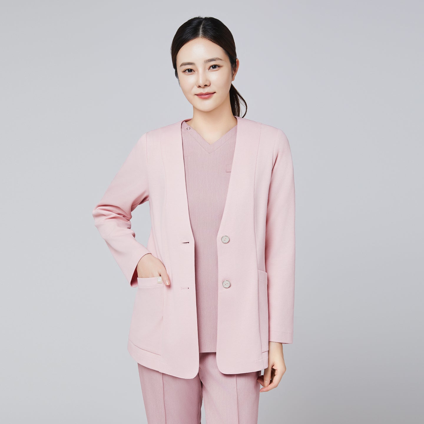 A woman wearing a soft pink comfort cardigan with button details, paired with matching trousers and a V-neck top, smiling confidently against a plain background,Soft Pink